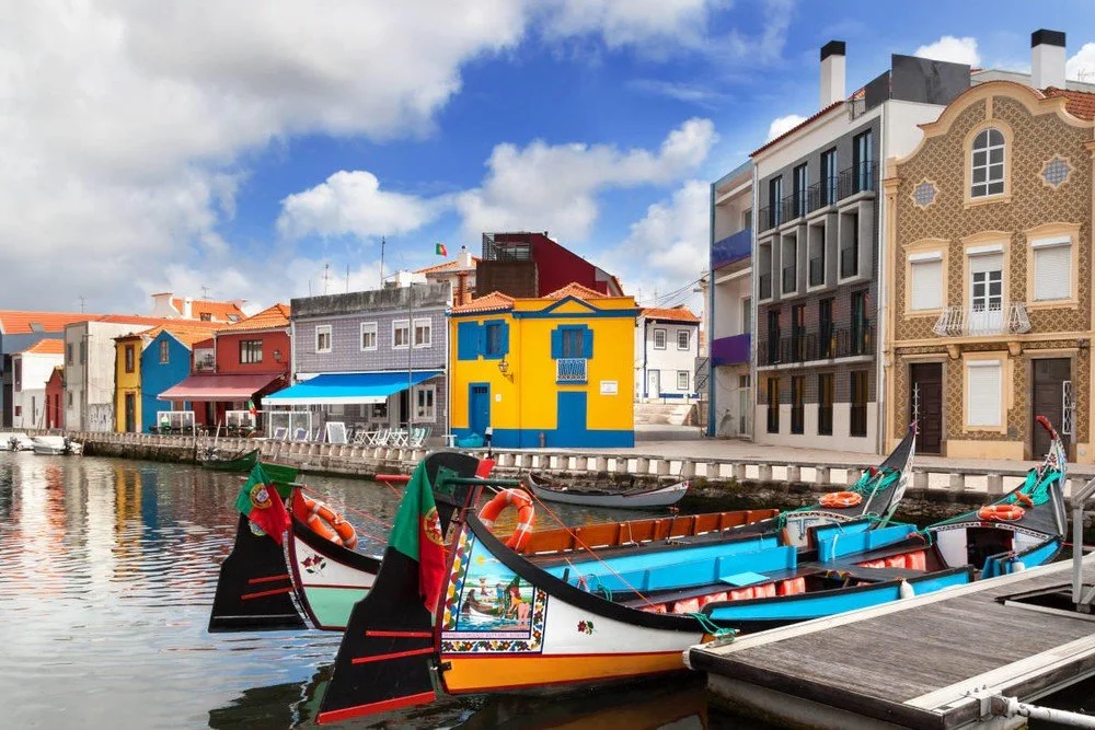 Scenic view of the canals of Aveiro, Portugal, featuring traditional moliceiro boats with colorful houses lining the canal. This picturesque setting captures the charm and beauty of Aveiro.