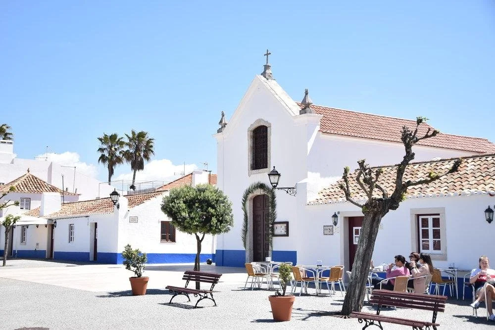 Whitewashed Igreja de Nossa Senhora da Soledade with blue trim in Porto Covo’s main square, Portugal.