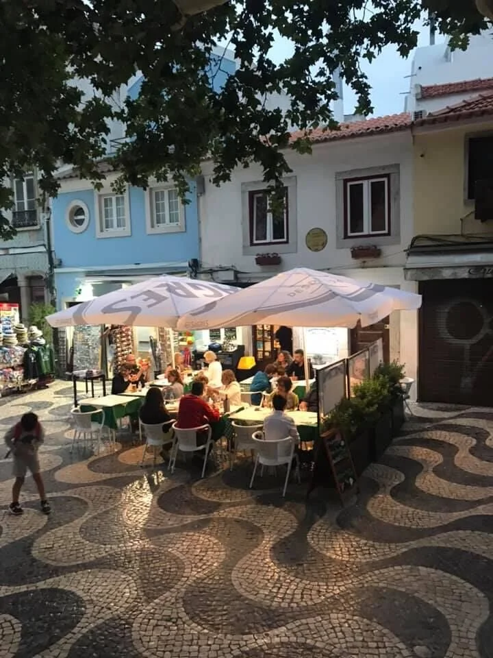 People enjoying traditional Portuguese food in the outdoor seating area of Taberna Económica de Cascais, a cozy, and authentic atmosphere tucked back among among traditional cobblestone streatts.