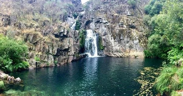 Canyoning Frades River: Scenic Waterfall Cascading into Clear Pool Surrounded by Rocky Cliffs and Lush Greenery.