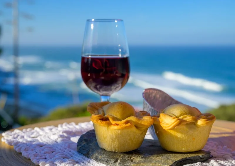 Traditional Portuguese empanadas paired with wine, with a scenic ocean view in the background.