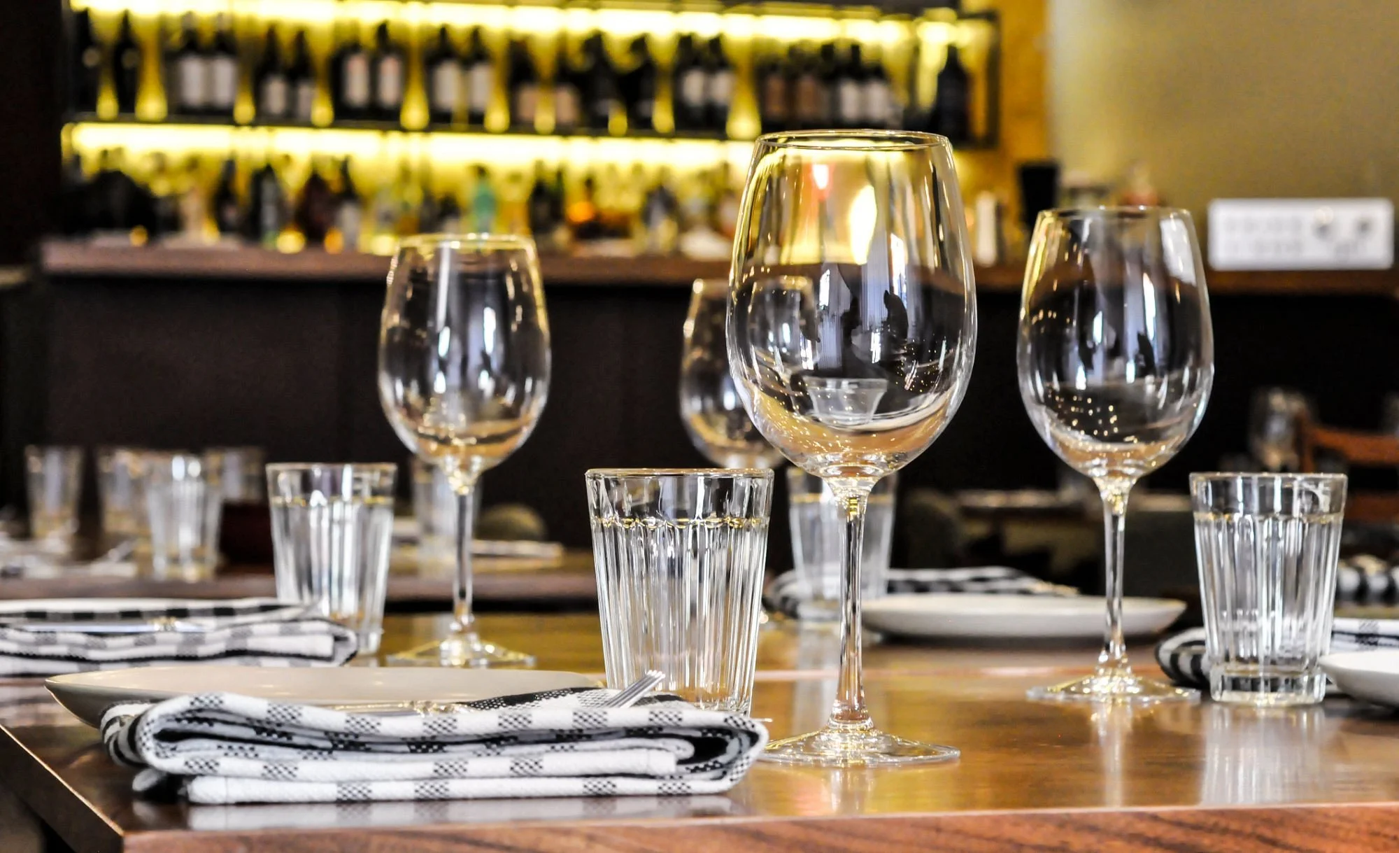 Mito Restaurante Porto offers a relaxed atmosphere with inviting Italian food, featuring a charming table setting with wine glasses, drinking glasses, and checkered napkins on a wooden table.