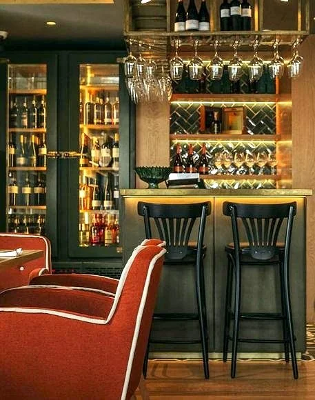 Cozy bar interior at Restaurante Casario Porto featuring wine bottles, hanging glasses, high stools, and red chairs.