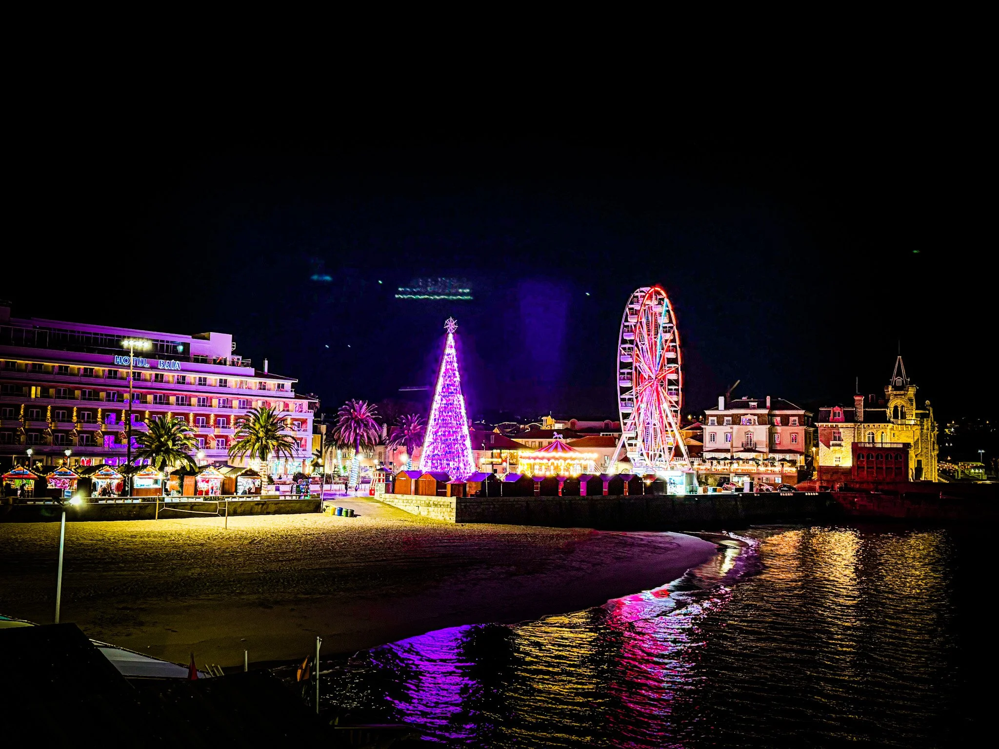 Cascais Christmas Bay at night with a Ferris wheel, illuminated Christmas tree and market stalls reflected on the wate