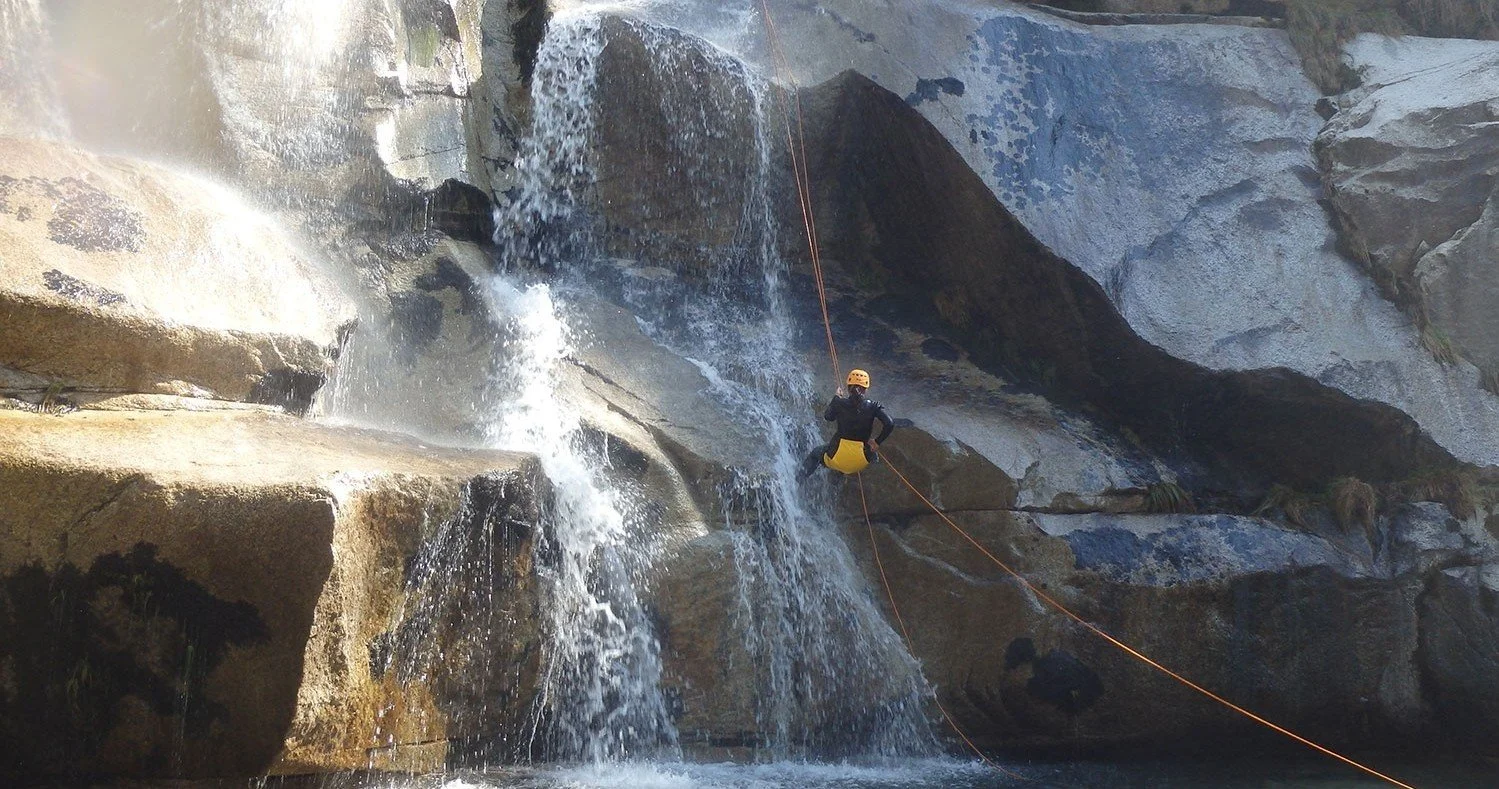 Person canyoning down a waterfall on the Paiva River using ropes, wearing a helmet and wetsuit.