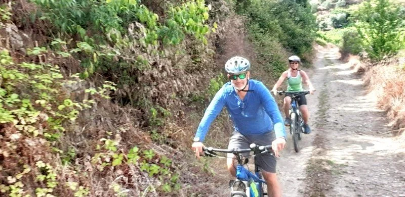 Two people biking on a dirt trail surrounded by greenery and trees in the Douro Valley.