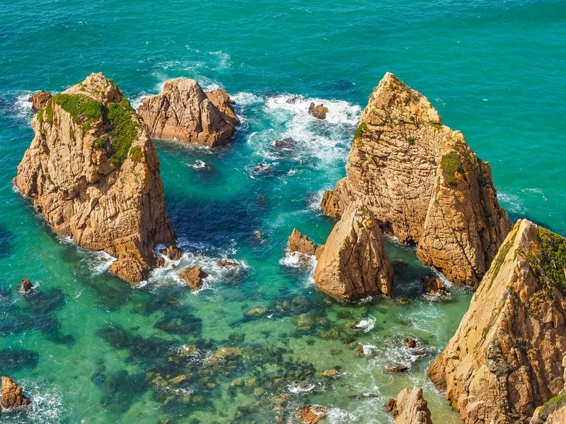 Aerial view of Praia de Ursa beach, featuring dramatic cliffs, golden sand, and jade colored waters in Portugal