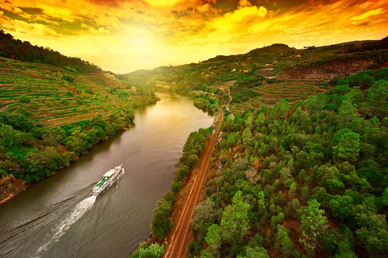 Boat gliding up the Douro River at sunset, surrounded by vineyards and terraced hills in Portugal