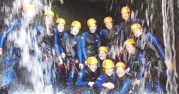 Canyoning Adventure Tour in Gerês National Park: Group of People in Wetsuits and Helmets Under a Waterfall.