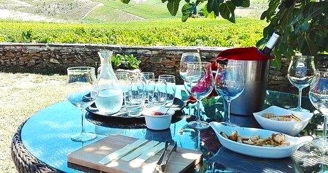 Outdoor table setting in the Douro Valley with wine glasses, ice bucket, cheese board, and scenic vineyard view in the background.