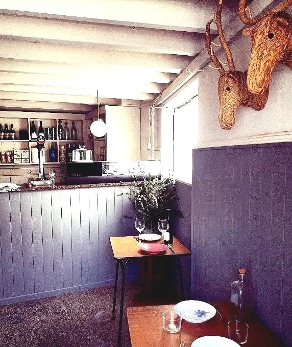 La Popular Taberna Ericeira: Cozy Cafe Interior with Wooden Tables, Wicker Animal Head Decor, and Bright Window, Featuring Counter with Bottles and Jar