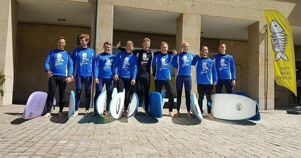 Porto Surf Camp: Group of Surfers in Blue Surf School Shirts Holding Surfboards on a Sunny Day.