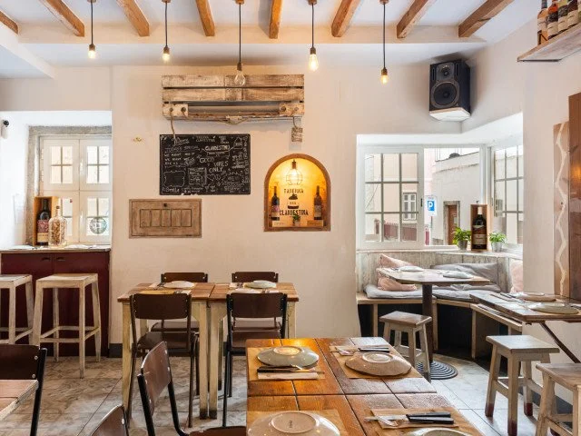 The interior of Clandestine Tavern Cascais exudes rustic charm with whitewashed walls and exposed wooden beams, creating a cozy and relaxing atmosphere. This inviting space is perfect for enjoying delicious tapas and cocktails with friends in a warm.