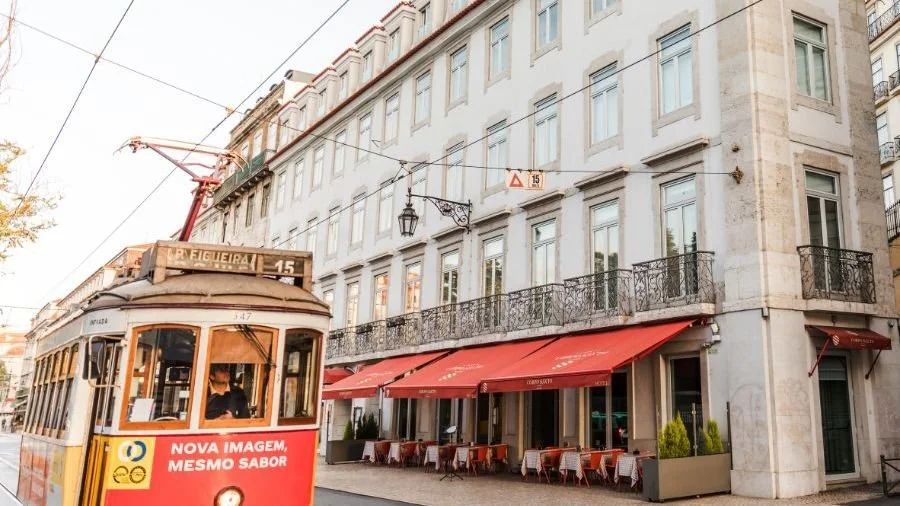 A historic yellow and red tram in Lisbon, Portugal, passes by the Corpo Santo hotel.