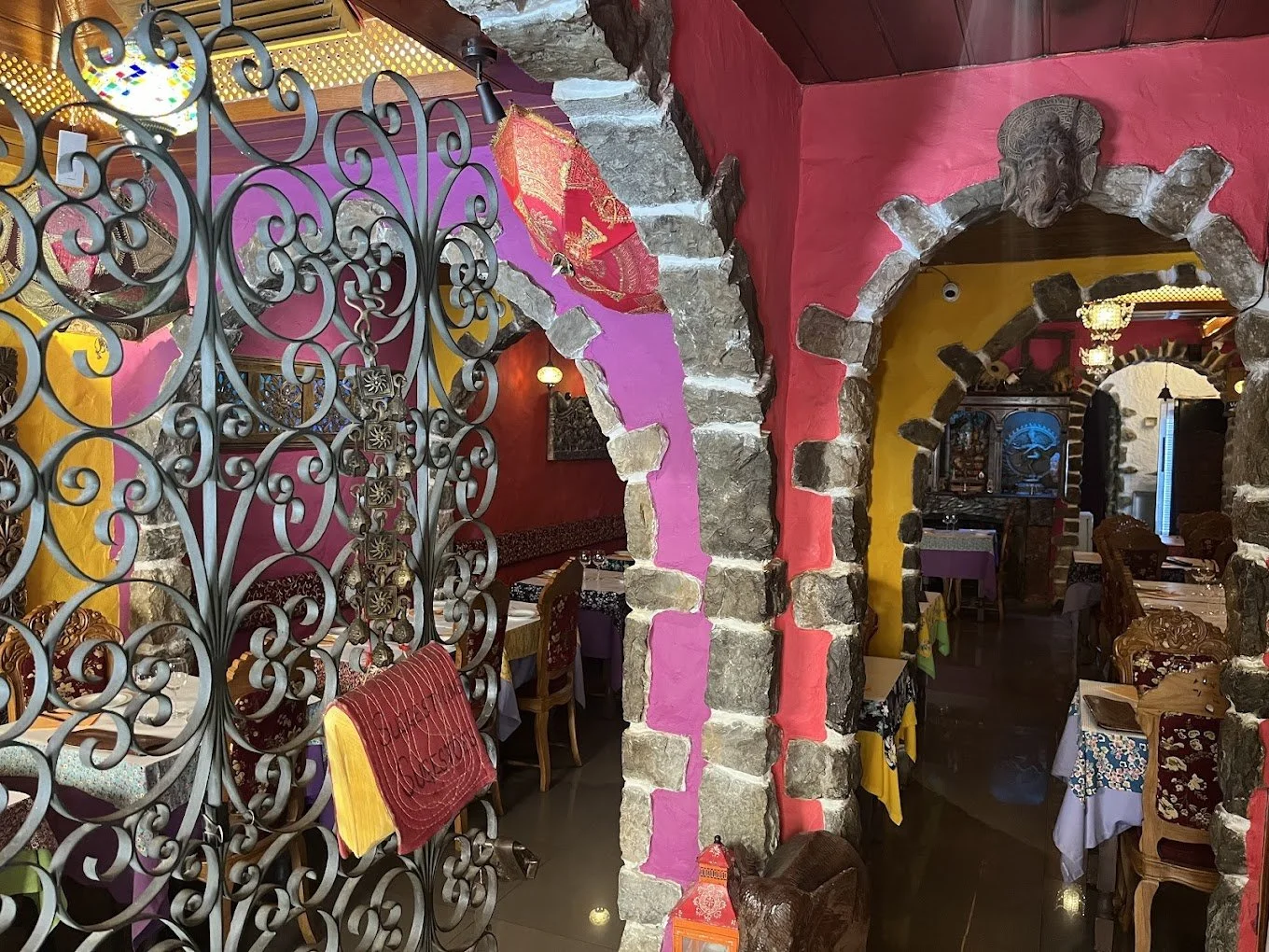 The colorful and vibrant entryway of Marsala Indian restaurant Cascais welcomes guests into a warm and inviting space, featuring wooden chairs, white tablecloths, and authentic tableware.