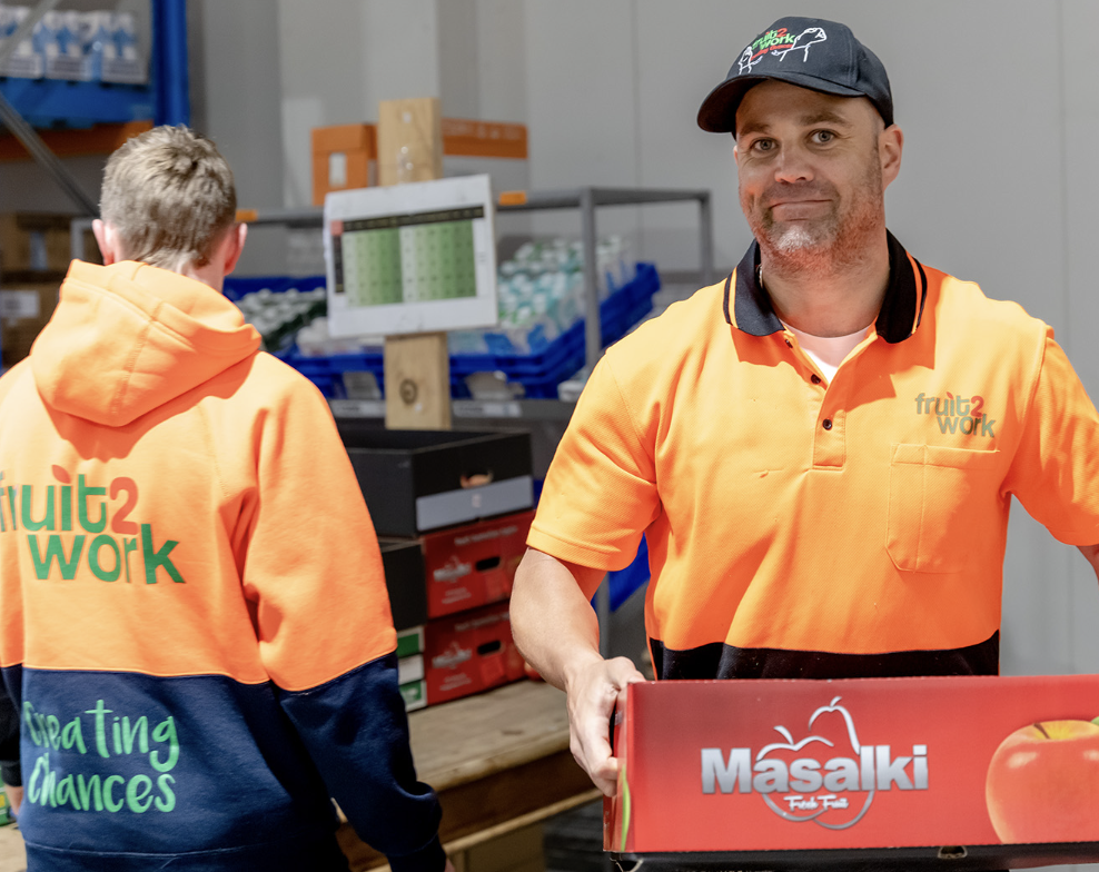 Two employees one facing the camera holding a box of fruit and the other with his back turned.