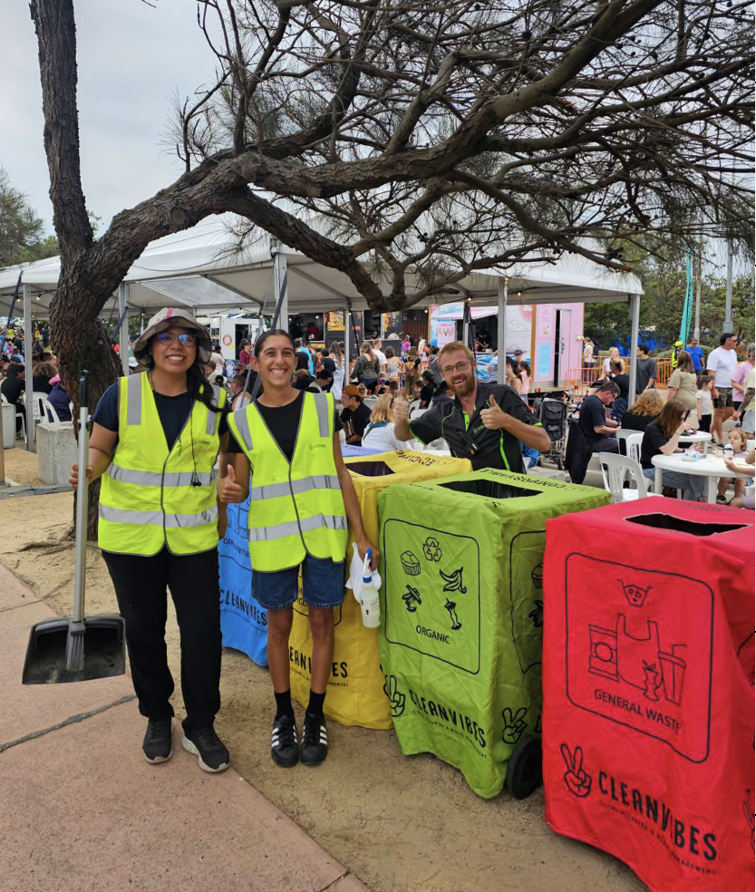 Two staff standing beside coloured wheelie bins with broom in hand smiling
