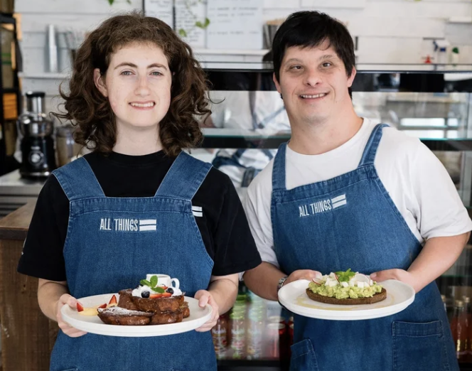 Two people living with disability standing smiling holding two plates of food.