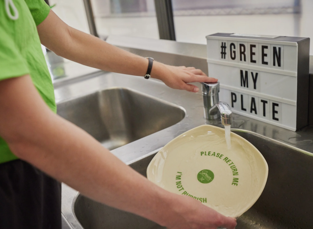 person washing reusable plate at a sink