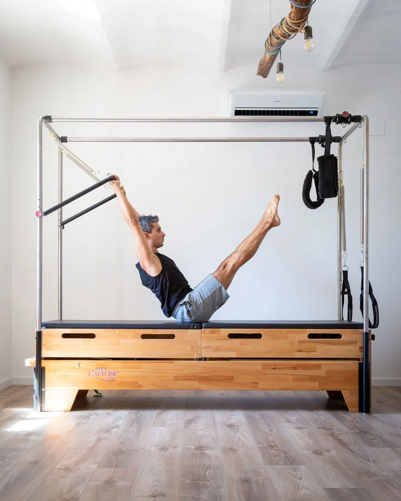 Persona che fa esercizi di pilates su un modulo con barre e anelli in una stanza luminosa.