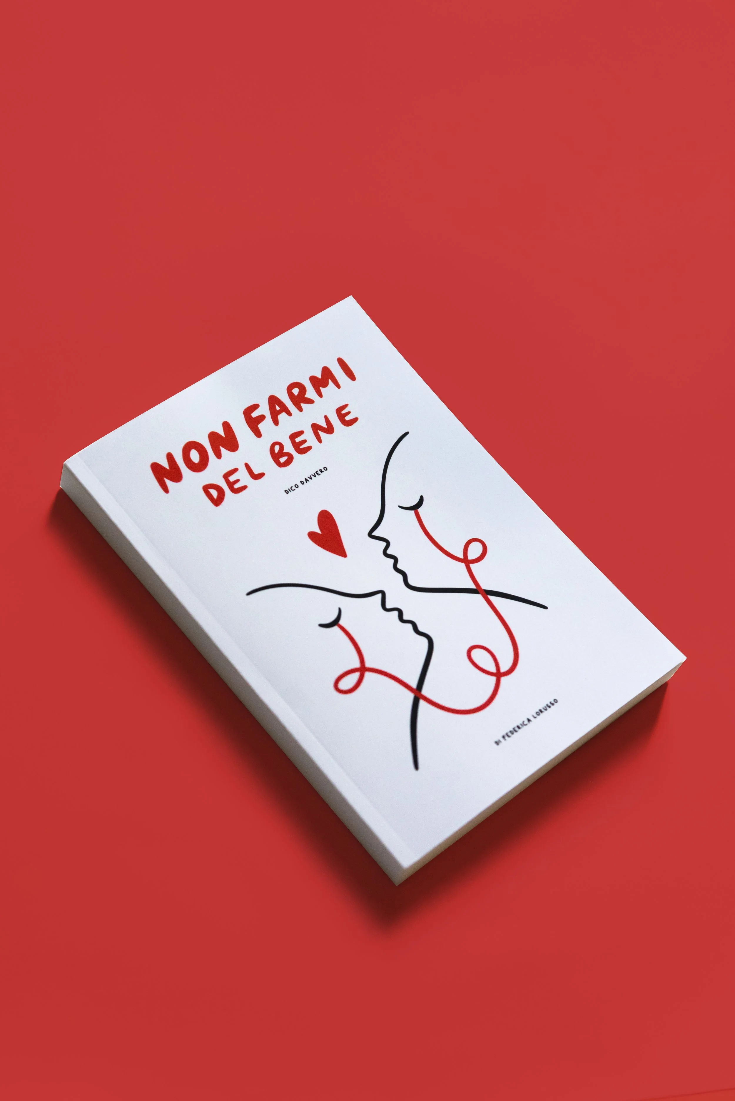 Copertina di un libro bianco con illustrazione di due profili di facce che si baciano, con una linea rossa che collega i due volti e forma un cuore, sullo sfondo rosso.