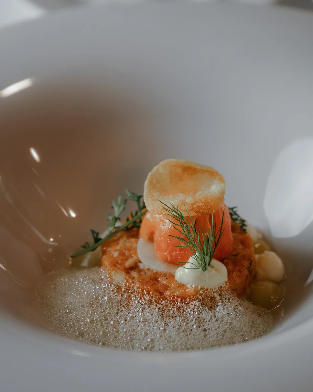 Feinsandiges Gericht mit einem Dip, einem Himbeerstück, einem Kräuterzweig, einem Knusperchip und einer schaumigen Sauce in einer weißen Schale. Restaurantfotografie Landgasthof Lamm in Ebnat.