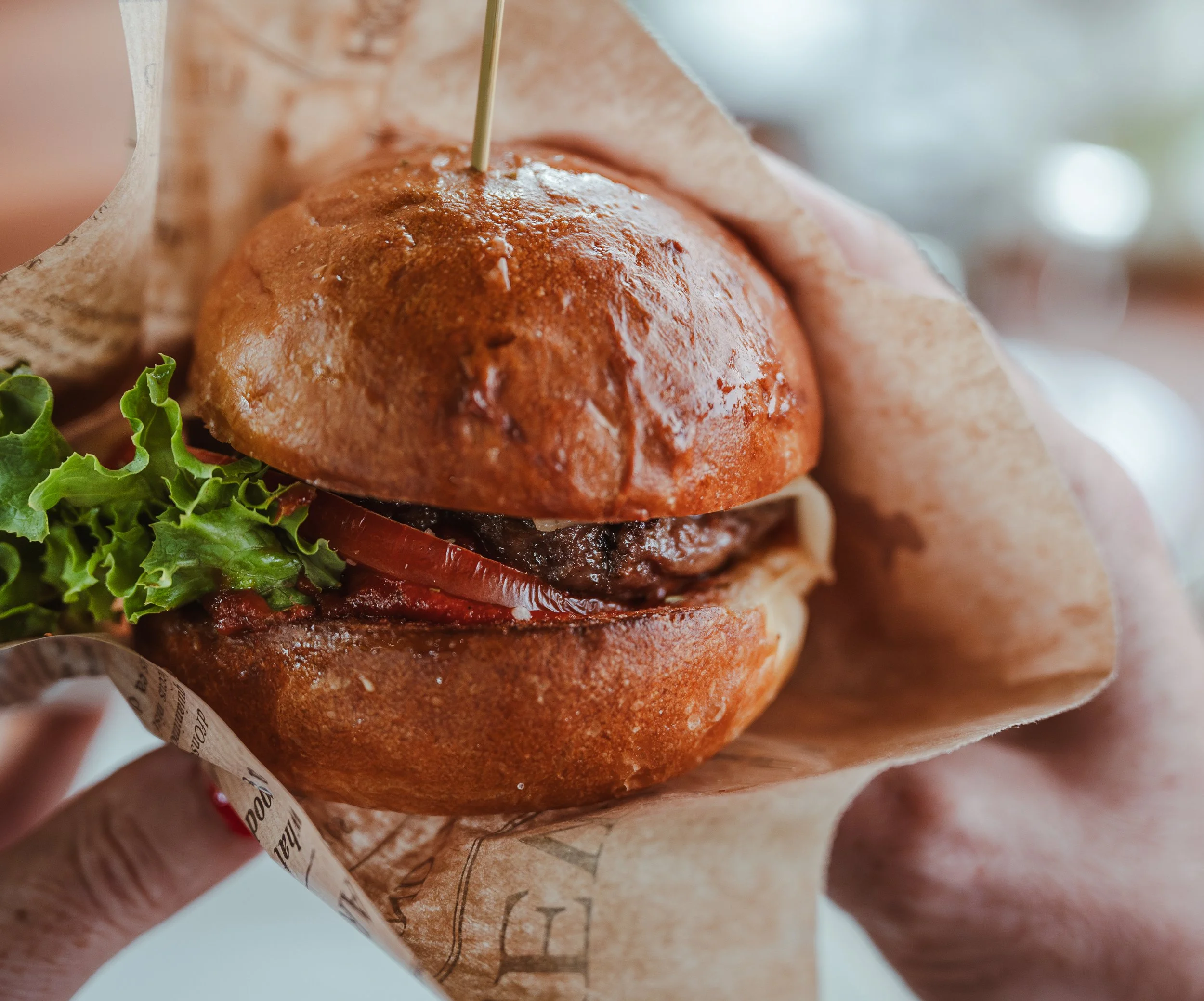 Ein Burger mit Rindfleischpatty, Tomate, Salat, Zwiebeln und Brötchen, eingewickelt in Zeitungspapier.