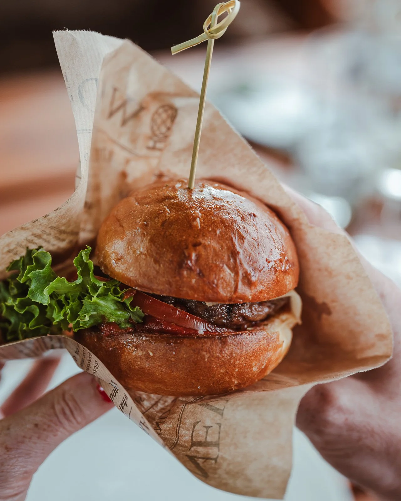 Hochwertiger Hamburger mit Salat, Zwiebeln und Tomaten, eingewickelt in Zeitungspapier und mit einem Zahnstocher.
