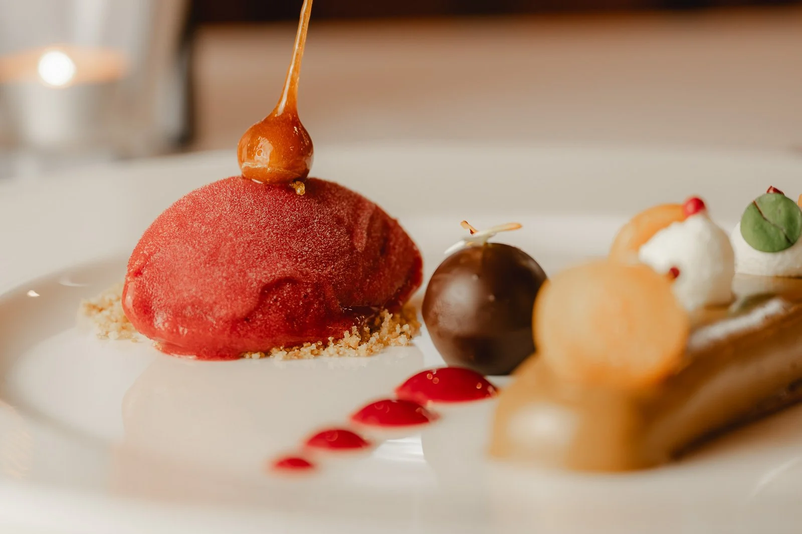 Elegantes Dessert mit roten Sorbet, Schokolade, Früchten und Dekorationen auf einem weißen Teller. Restaurantfotografie Landgasthof Lamm in Ebnat.