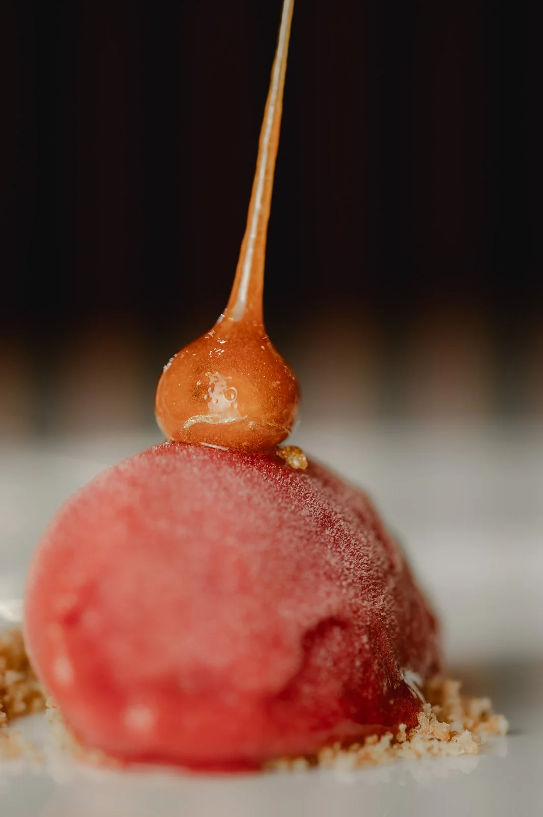 Nahaufnahme eines essbaren Desserts mit roter Kugel, die mit einer dünnen, glänzenden Karamellschicht bedeckt ist, und einer goldbraunen Karamellglage, die auf der roten Kugel platziert ist. Restaurantfotografie Landgasthof Lamm in Ebnat.