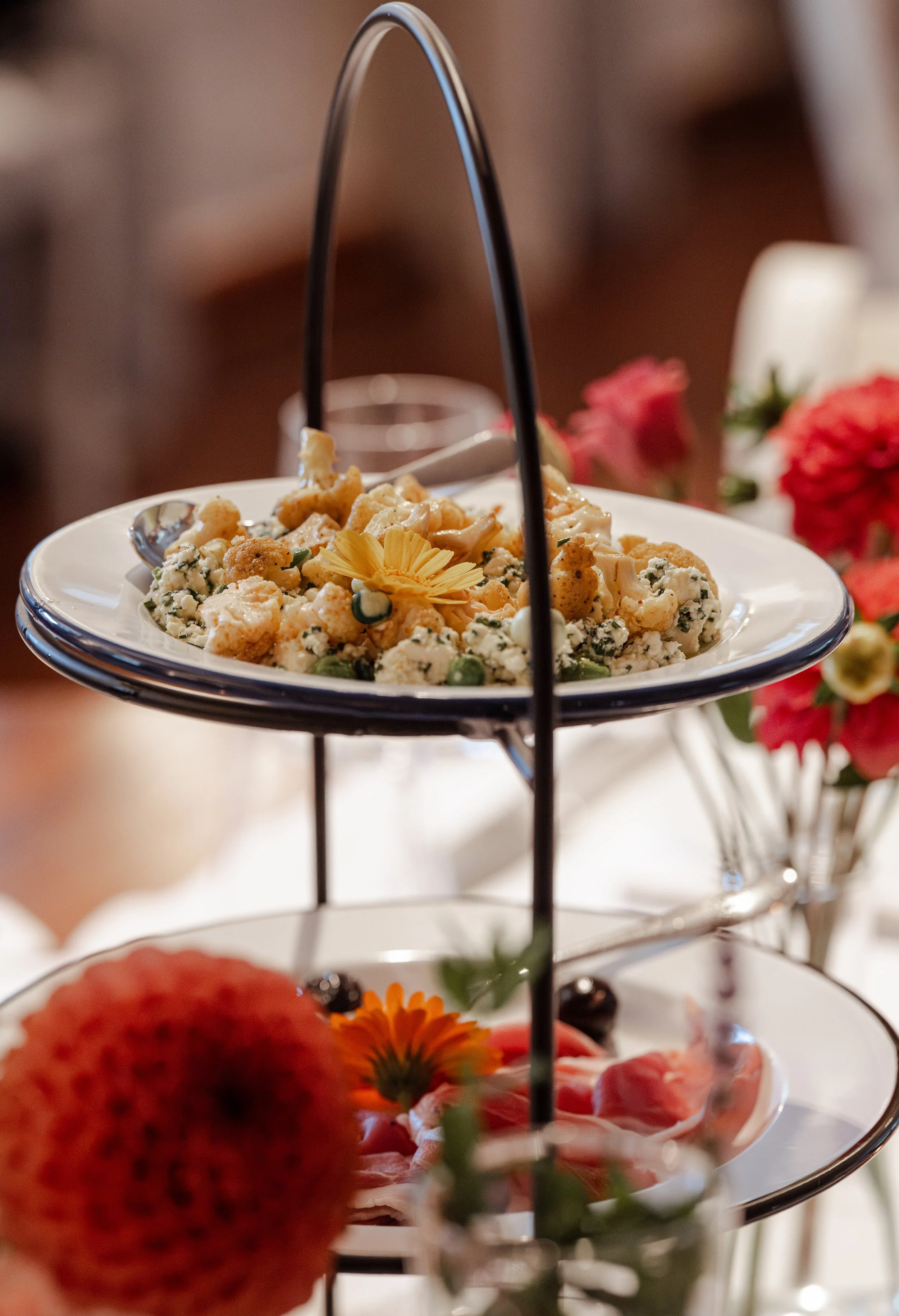 Ein zweistöckiges Desserttablett mit Salat und Blumen, dekoriert mit Blumen und Früchten, auf einem festlichen Tisch.