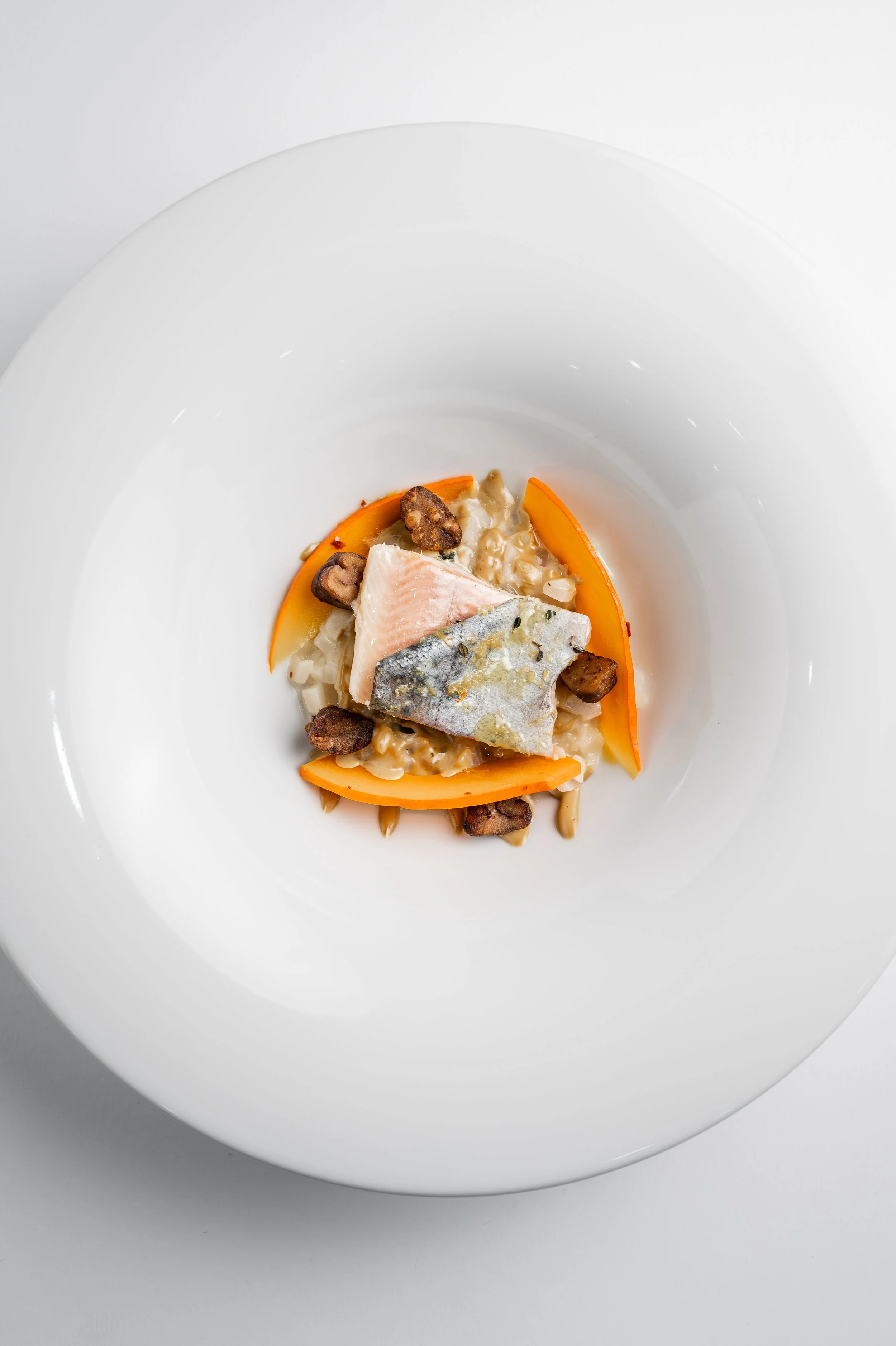 Teller mit einem Fisch, Karotten, Nüssen und cremiger Soße Gericht.