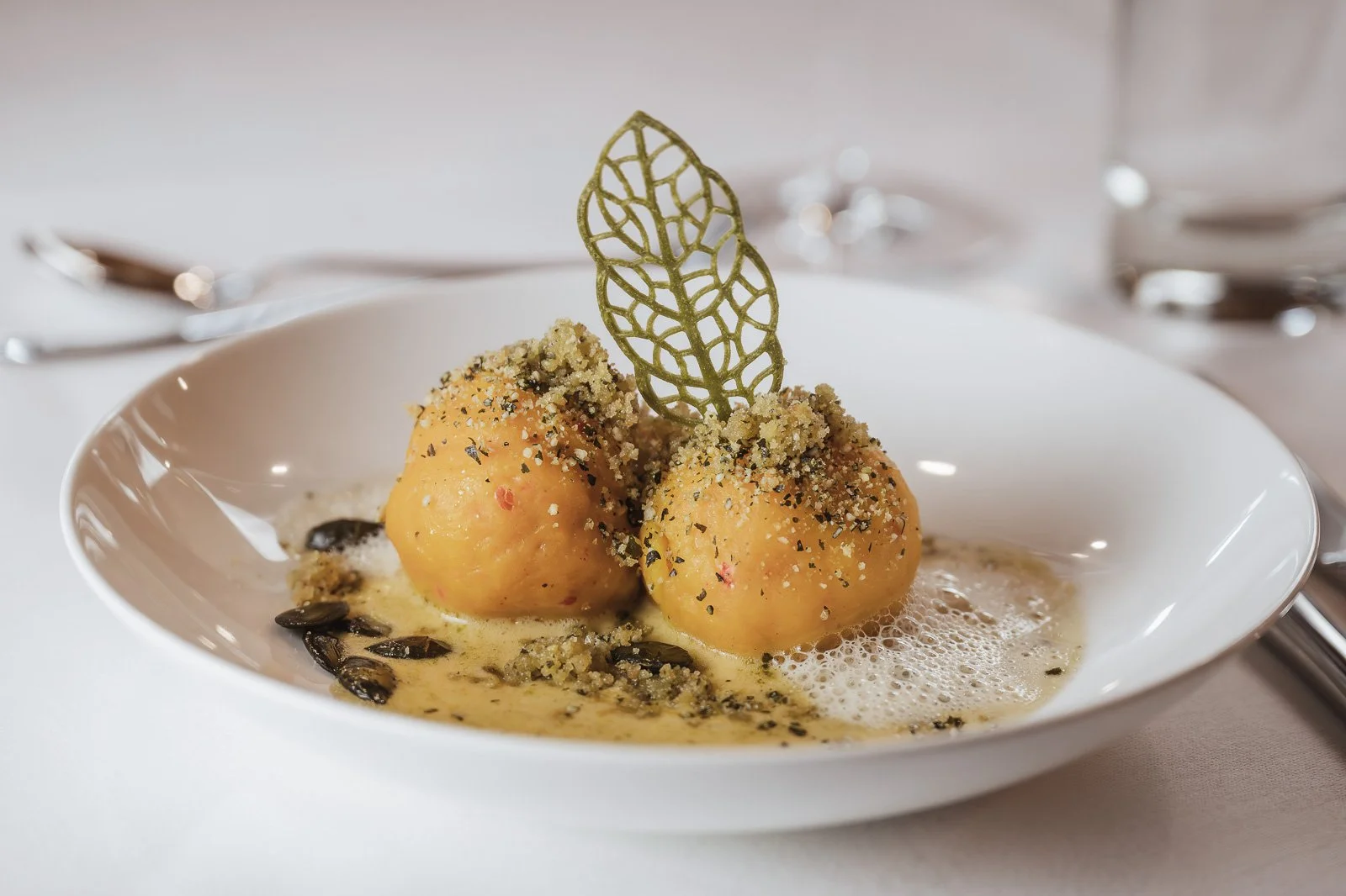 Gedeckte Kartoffelknödel mit Kräuterfüllung, serviert in einer weißen Schüssel mit Tomatensoße, garniert mit einem dekorativen Blatt aus essbarem Gold. Restaurantfotografie Landgasthof Lamm in Ebnat.