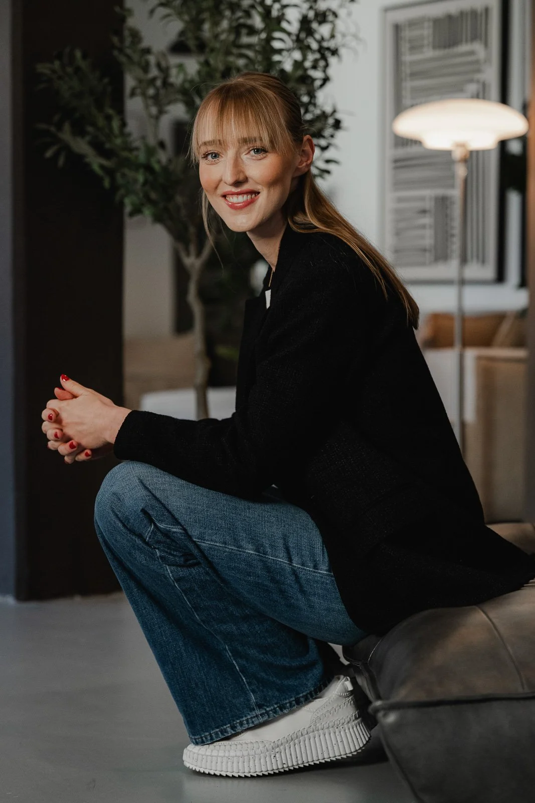Business-Porträtfotografie in Schwäbisch Gmünd – junge Businessfrau mit blonden Haaren, in schwarzen Jacke und blauer Jeans, lächelnd im Studio sitzend.