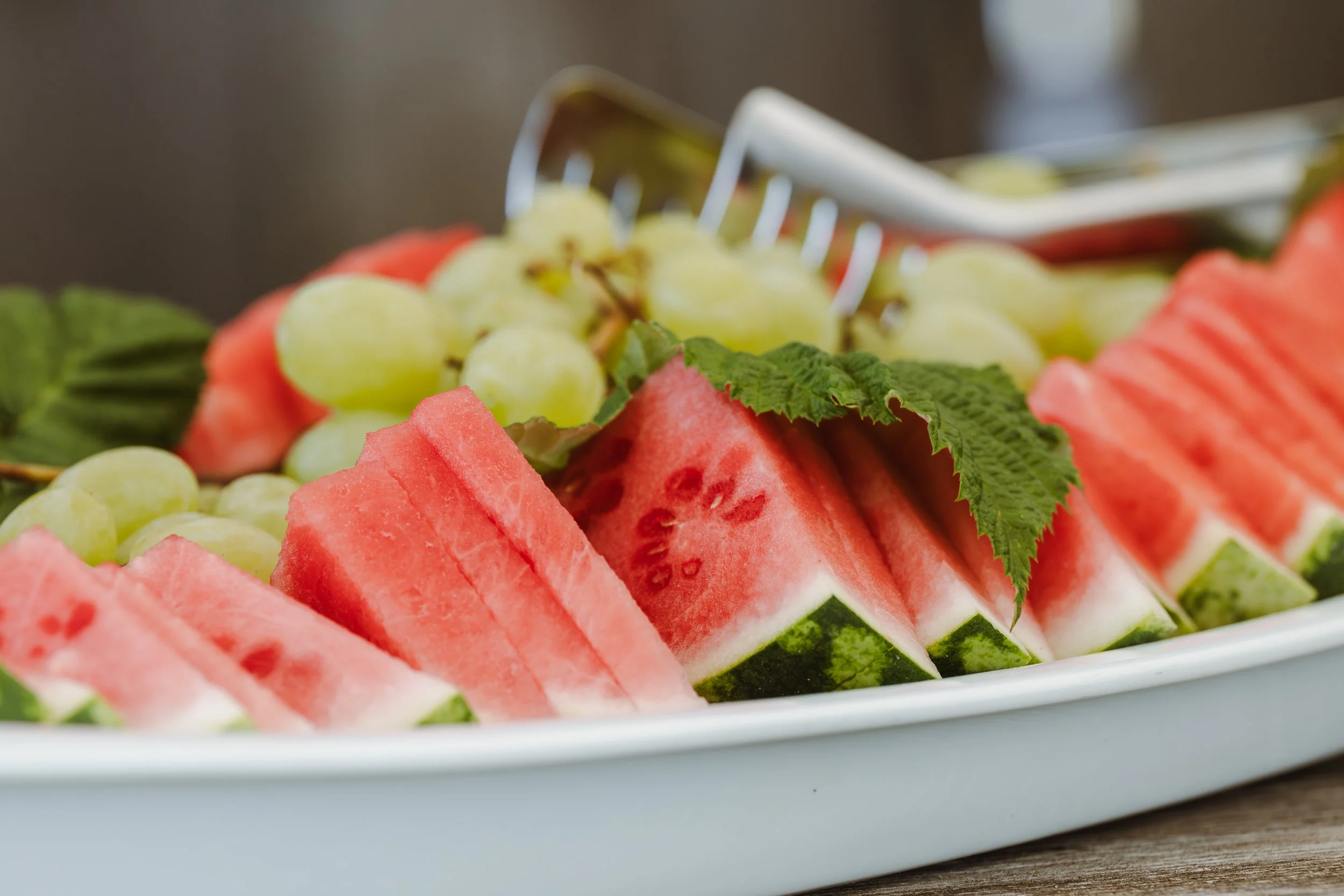 Frisches Obst mit Wassermelone, grüner Weintraube und Weinblättern auf einem weißen Teller.
