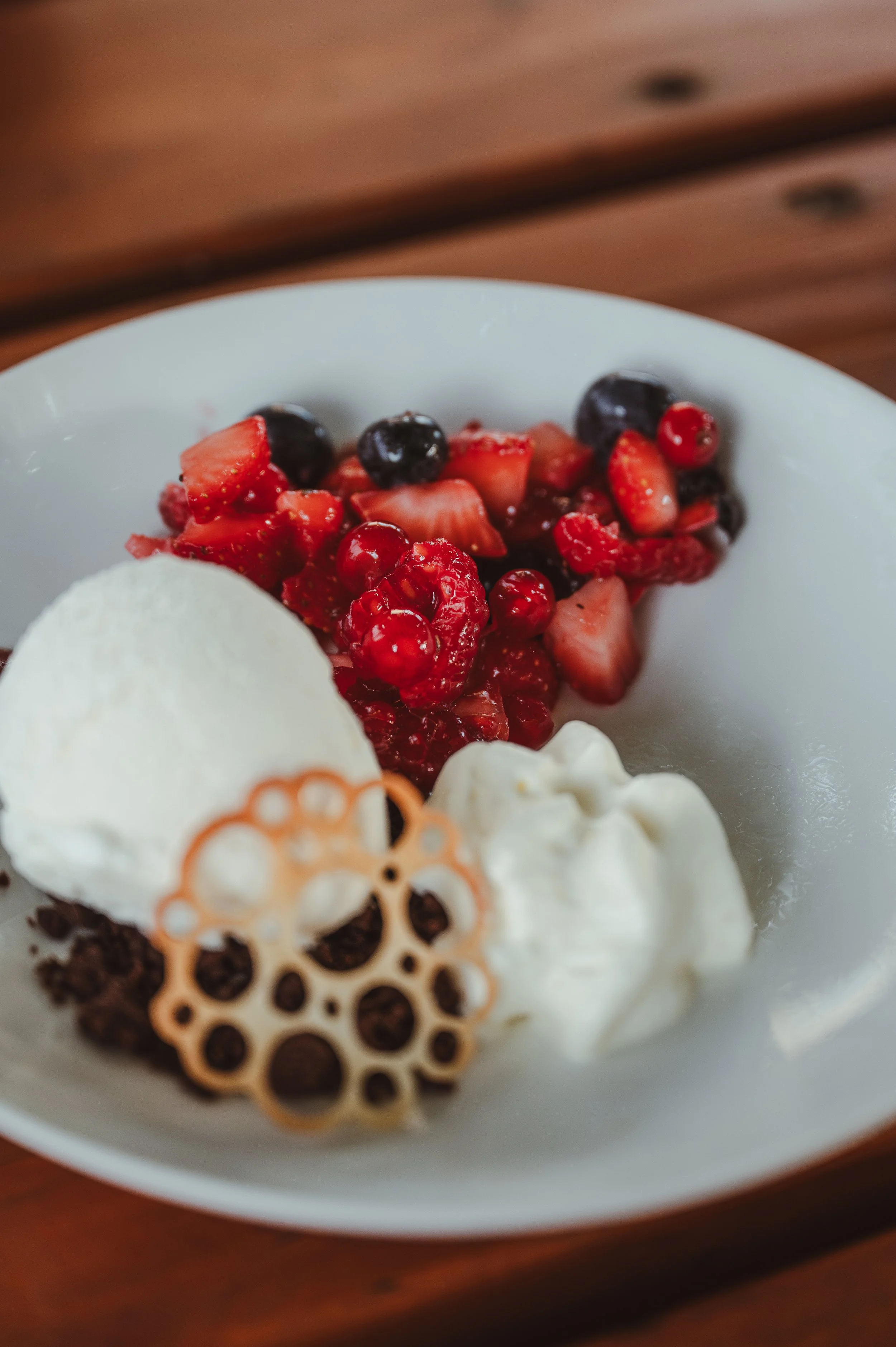 Eine Schüssel mit gemischtem Obst, Sahne, einer Kugel Vanilleeis und einem dekorativen Keks auf einem Holztisch.