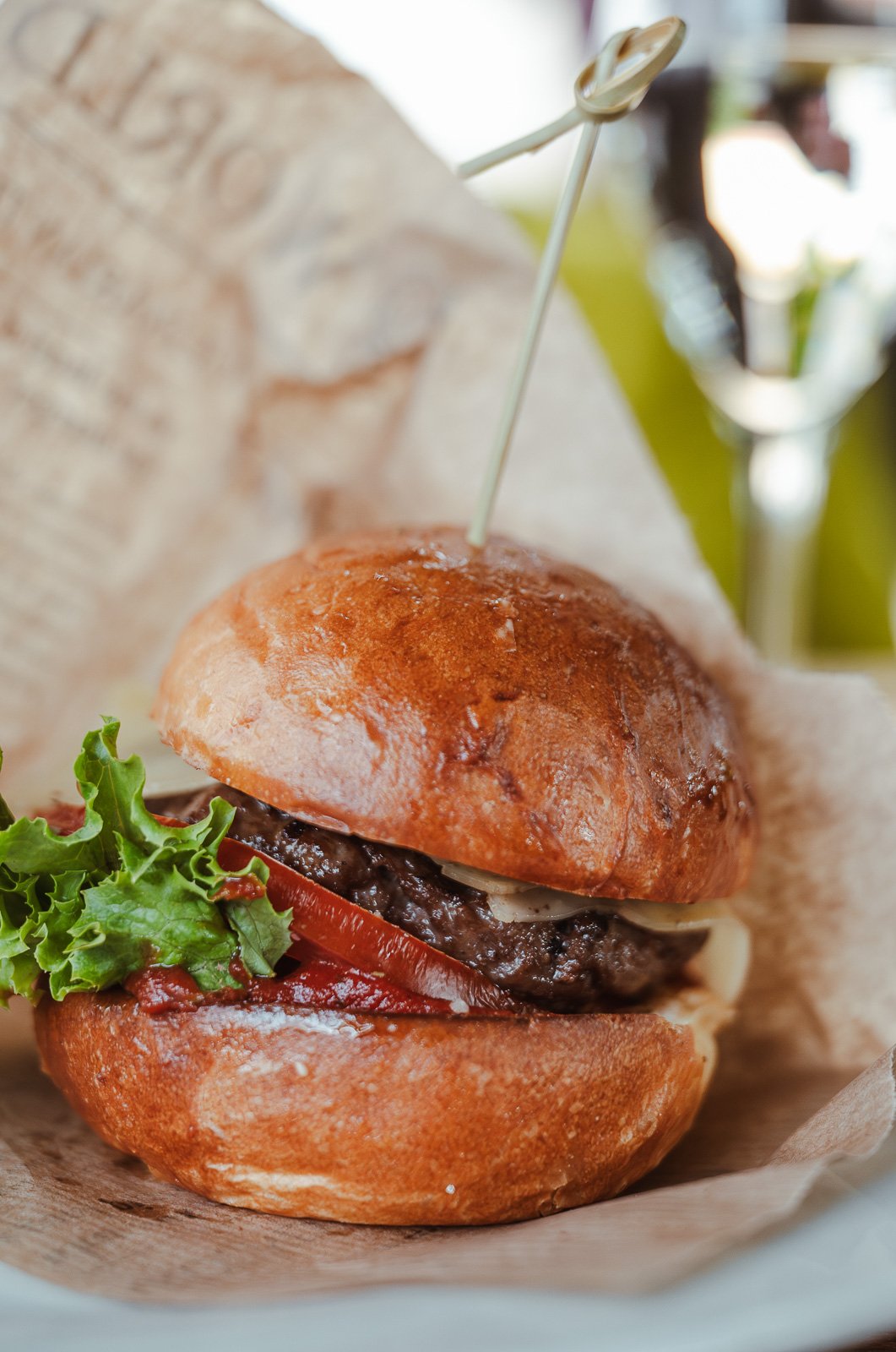 Ein Hamburger mit Rindfleischpatty, Salat, Tomaten, Käse, und Brötchen, serviert auf Pergamentpapier.