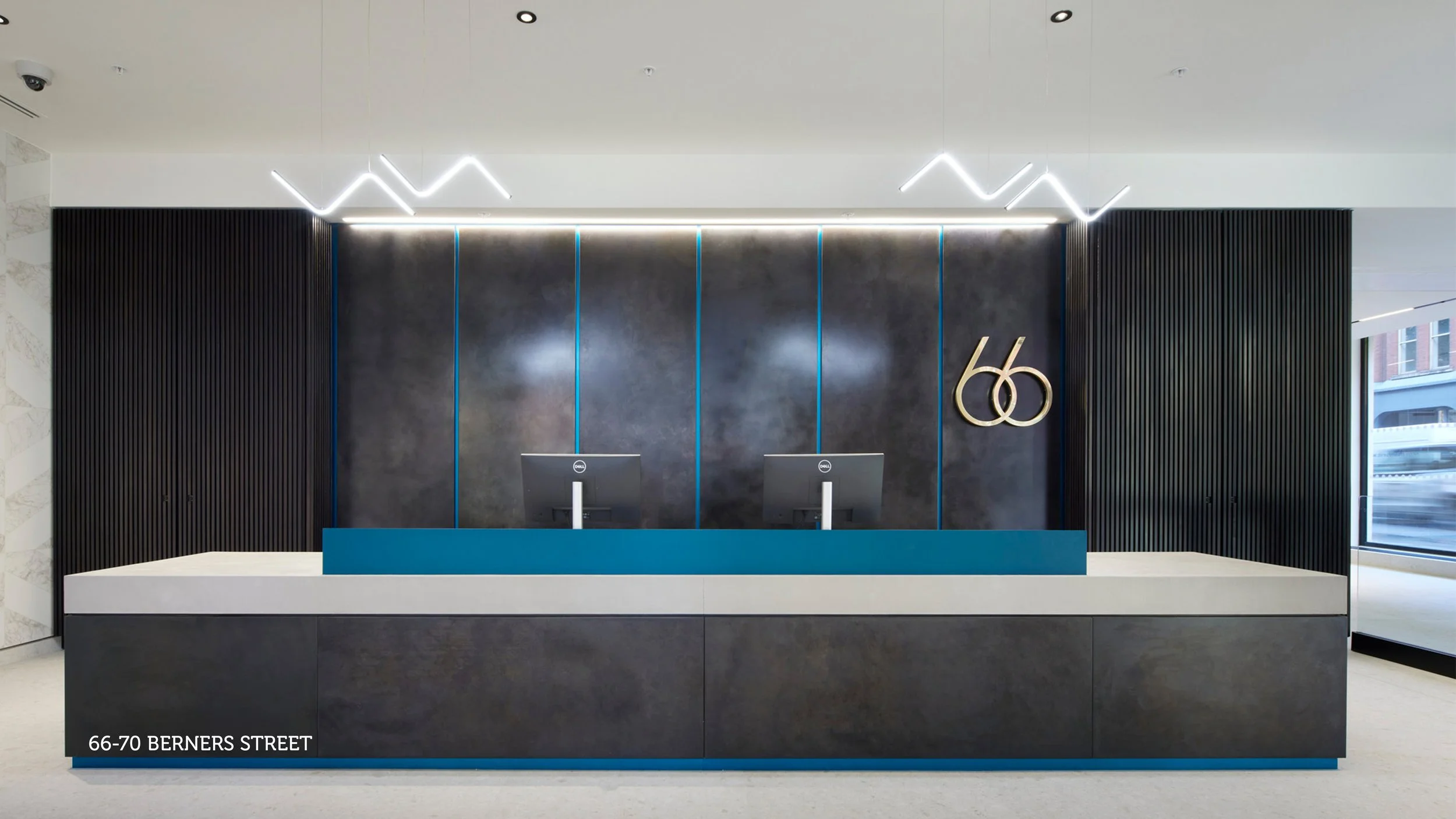Modern hotel or office reception area with a curved front desk, black chairs, orange benches near windows, and decorative lighting on a wooden panel wall.
