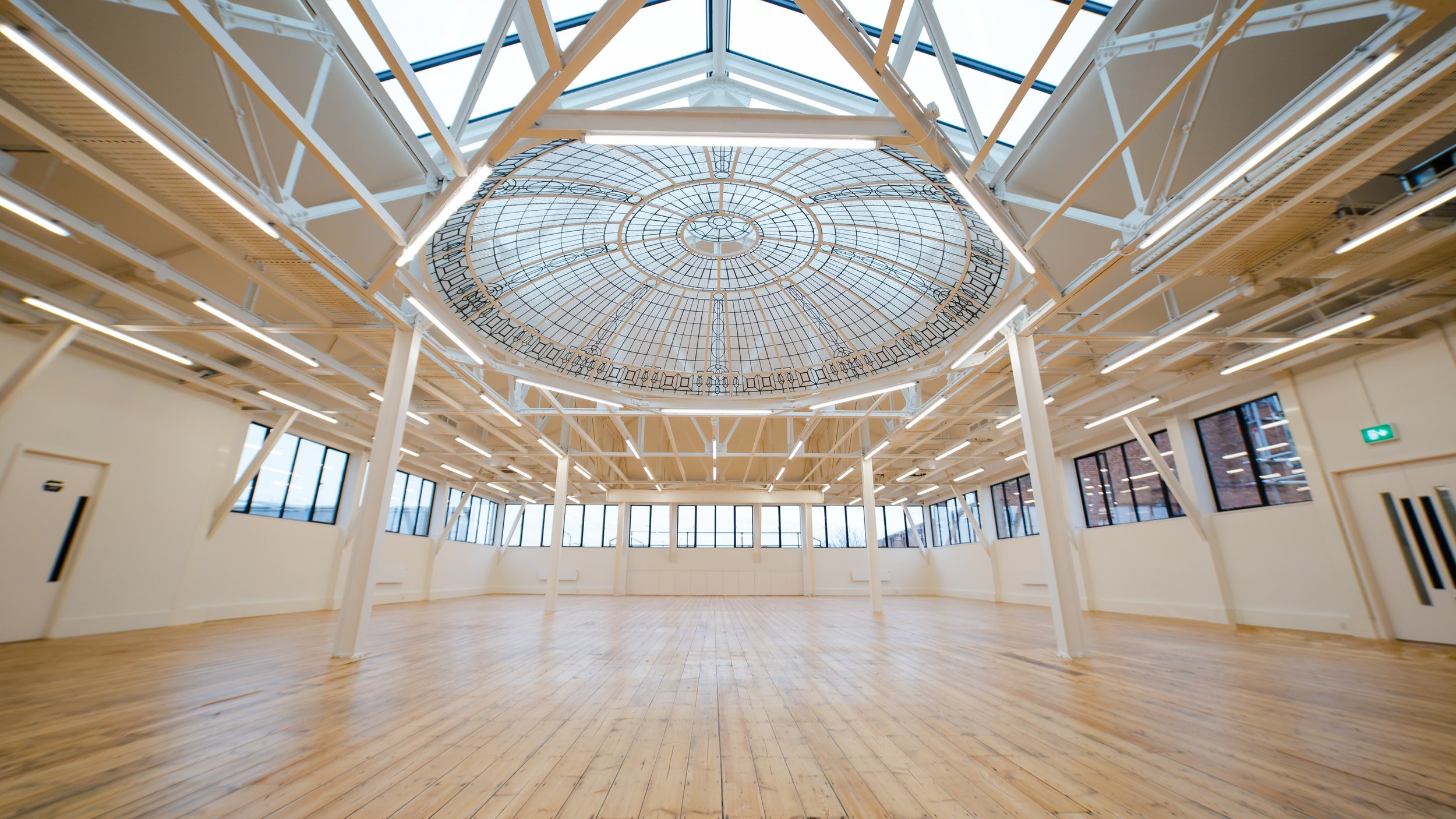 Empty room with a wooden floor, large windows, and a glass ceiling with intricate metalwork.