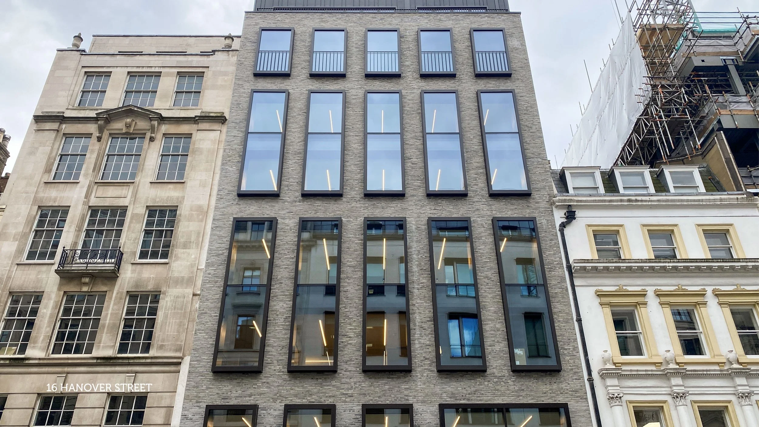 Modern office space with large windows offering city skyline views, blue chairs, and wooden storage units, featuring a glass railing around an open staircase.