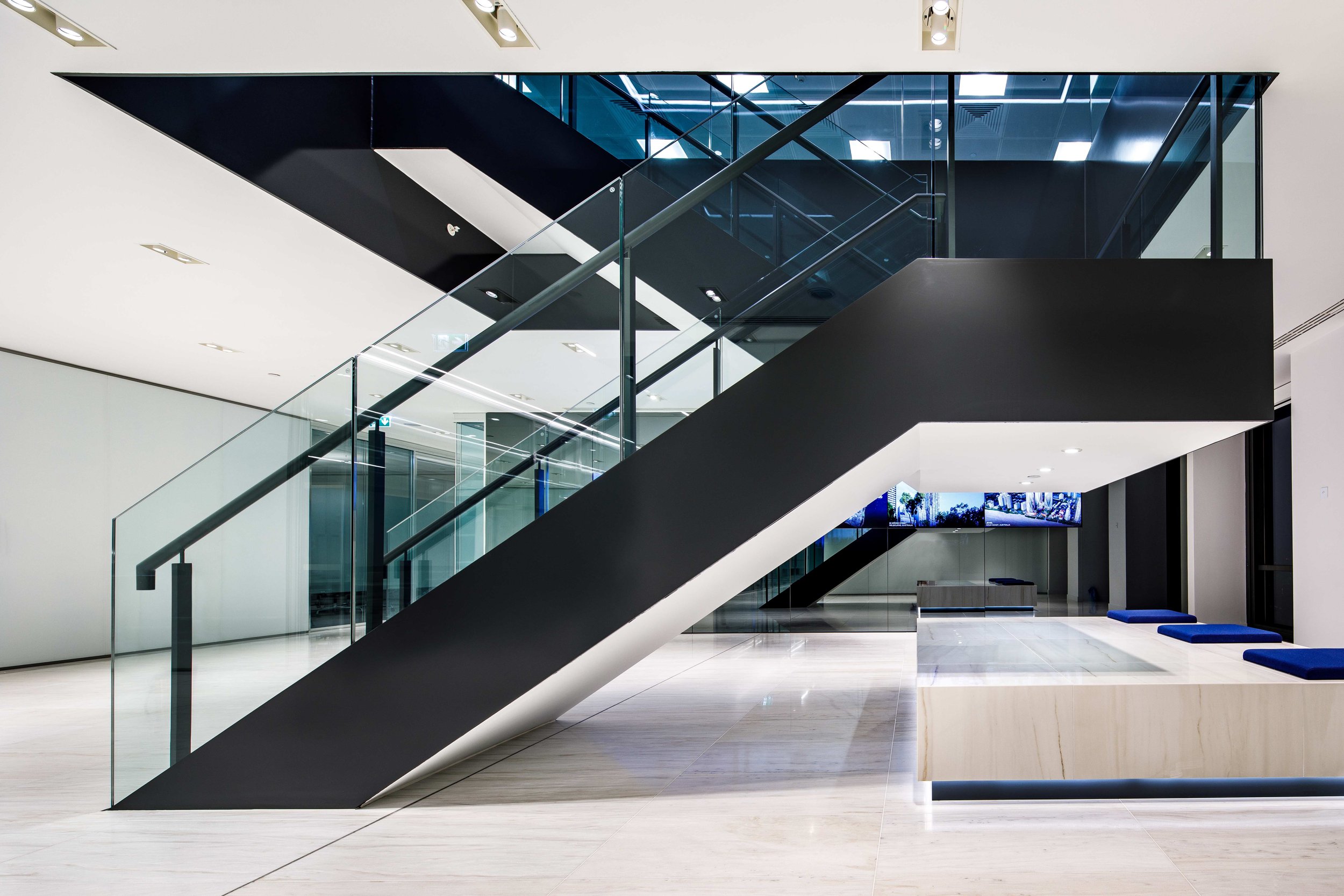 Modern interior lobby with a black and glass staircase and a reception desk with blue cushions.