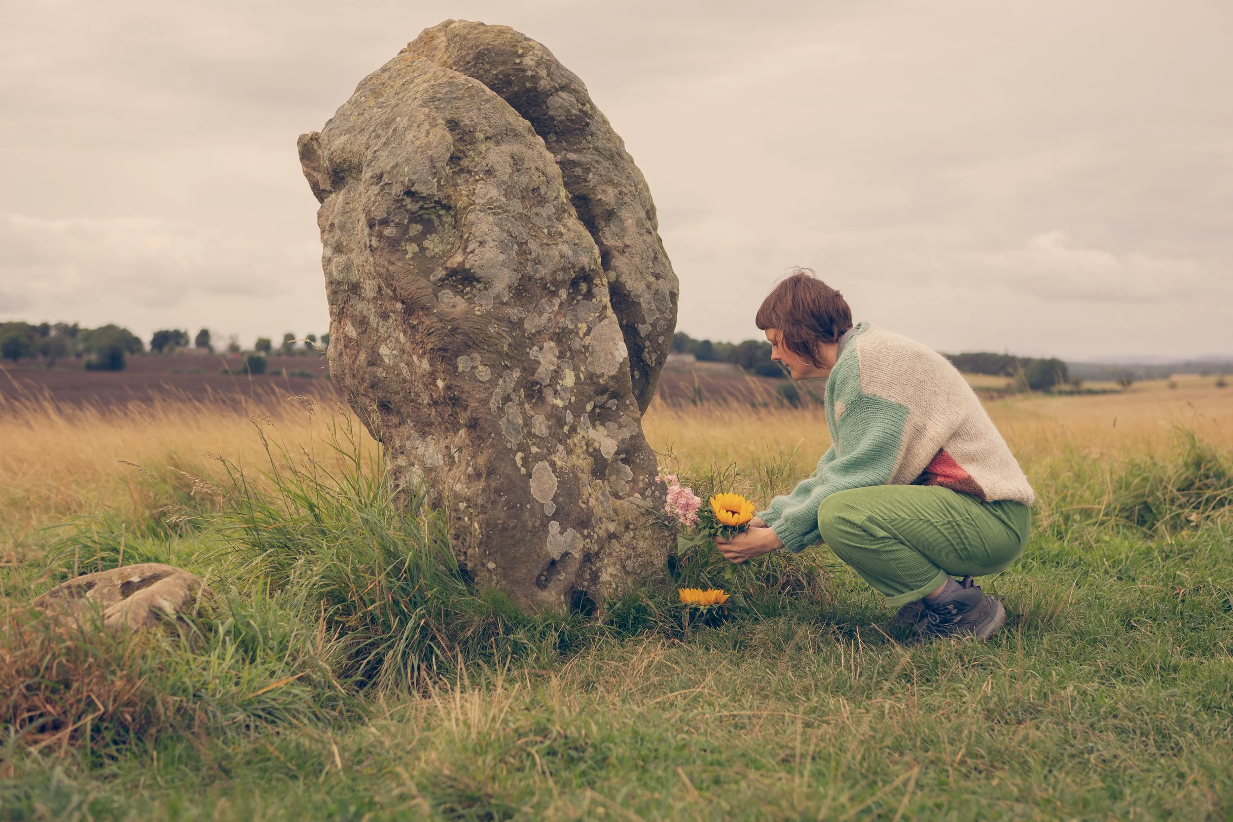 Beth places a sunflower at the base of a standing stone in Northumberland