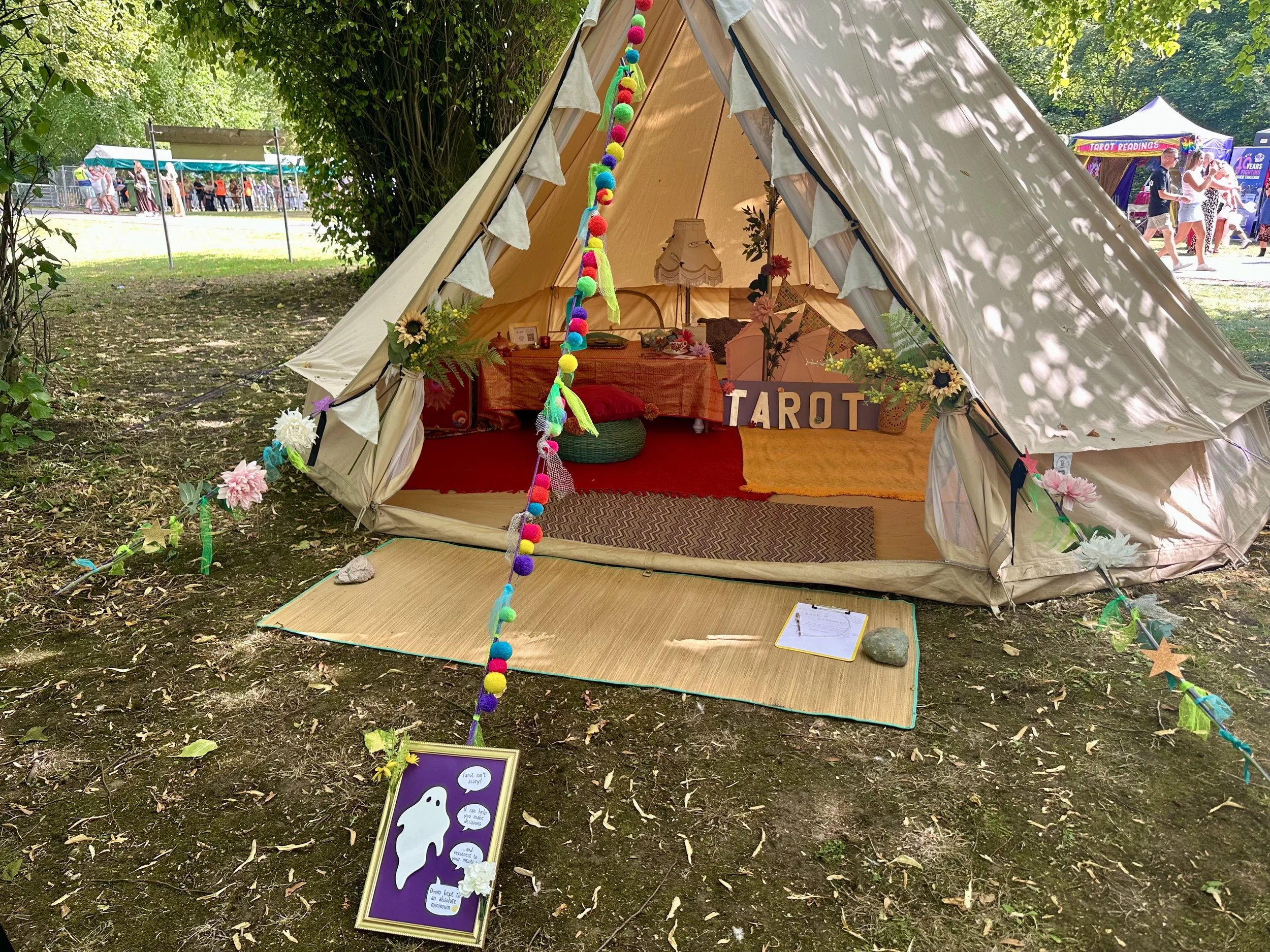 Beth's Tarot tent at a festival. It is a natural canvas bell tent, decorated with colourful garlands