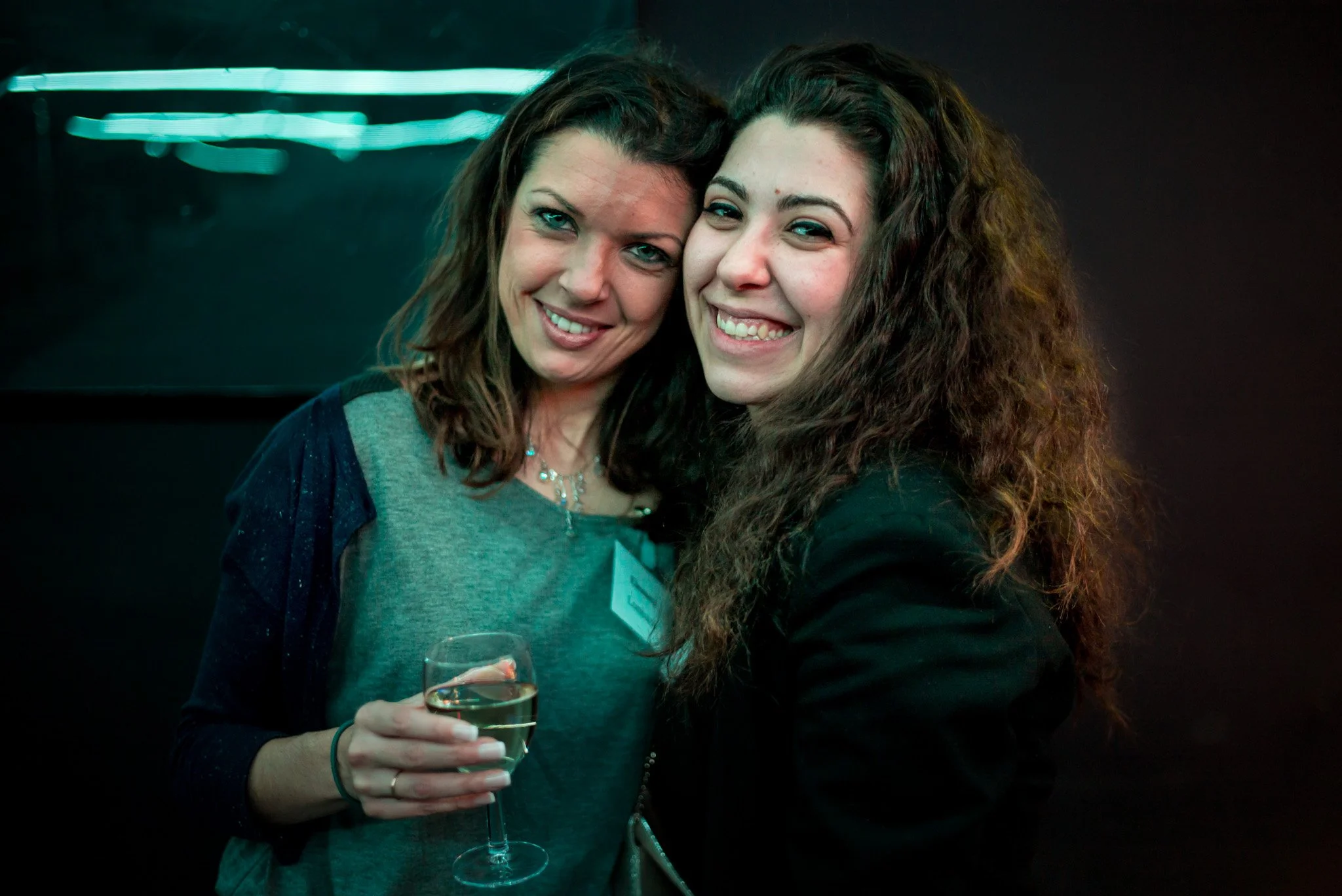 Deux femmes souriantes partagent un moment de complicité lors de la soirée Régus. Verres de vin à la main, ambiance chaleureuse et lumineuse, représentant les connexions humaines au cœur de l'événement.