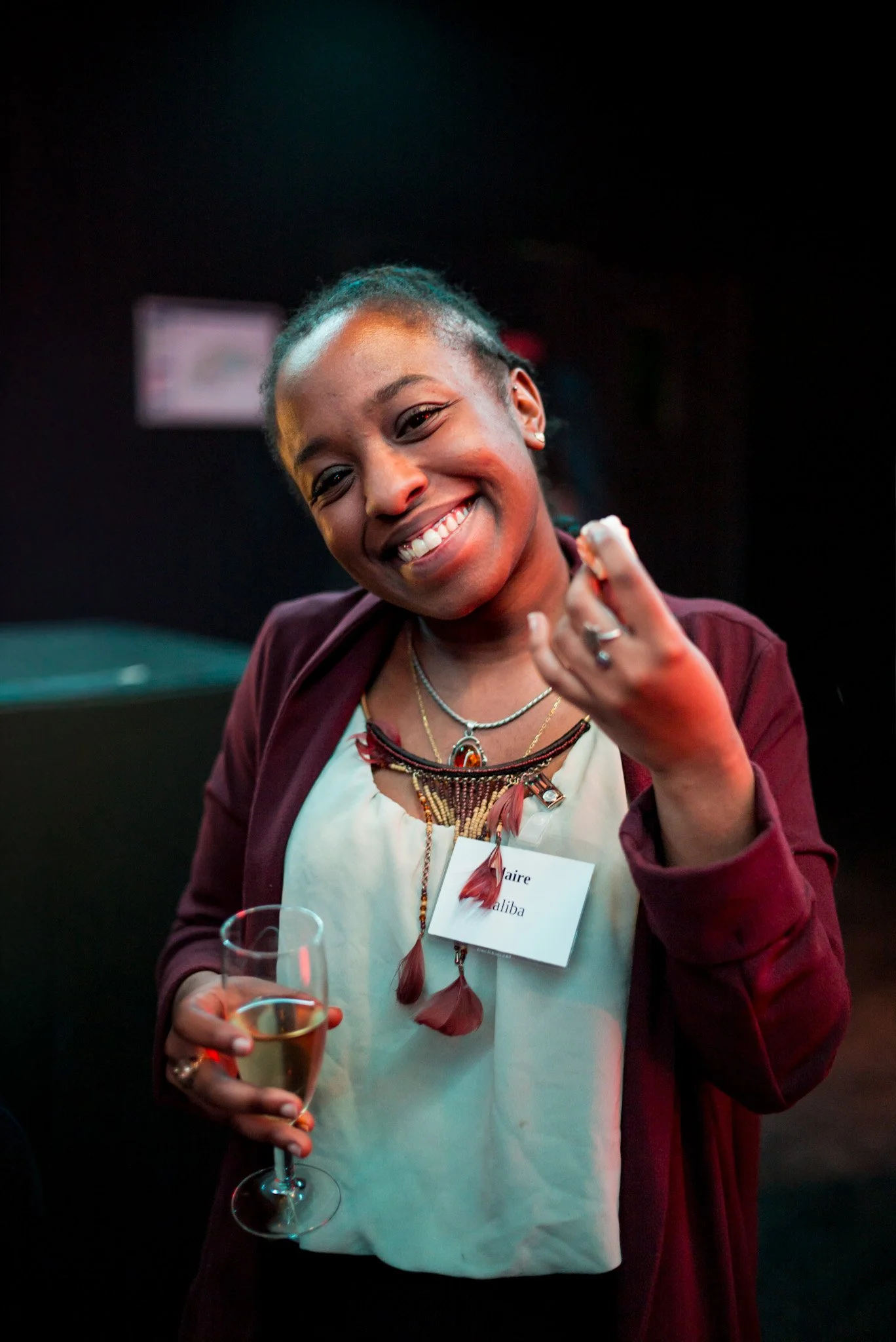 Claire Haliba sourit joyeusement en levant son verre lors de la soirée Régus Paris. Bijoux ethniques et ambiance colorée, représentant la diversité et la convivialité des participants de l'événement.