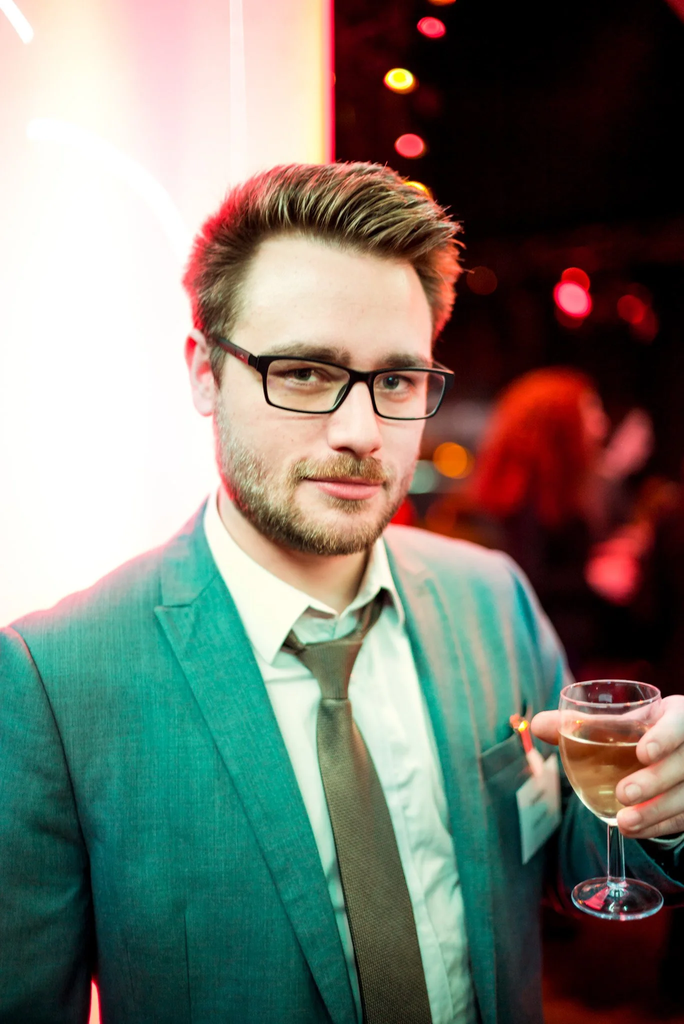 Un homme en costume tient un verre de champagne lors de la soirée Régus Paris. Éclairage coloré et ambiance sophistiquée, représentant l'élégance et le style des invités de l'événement.