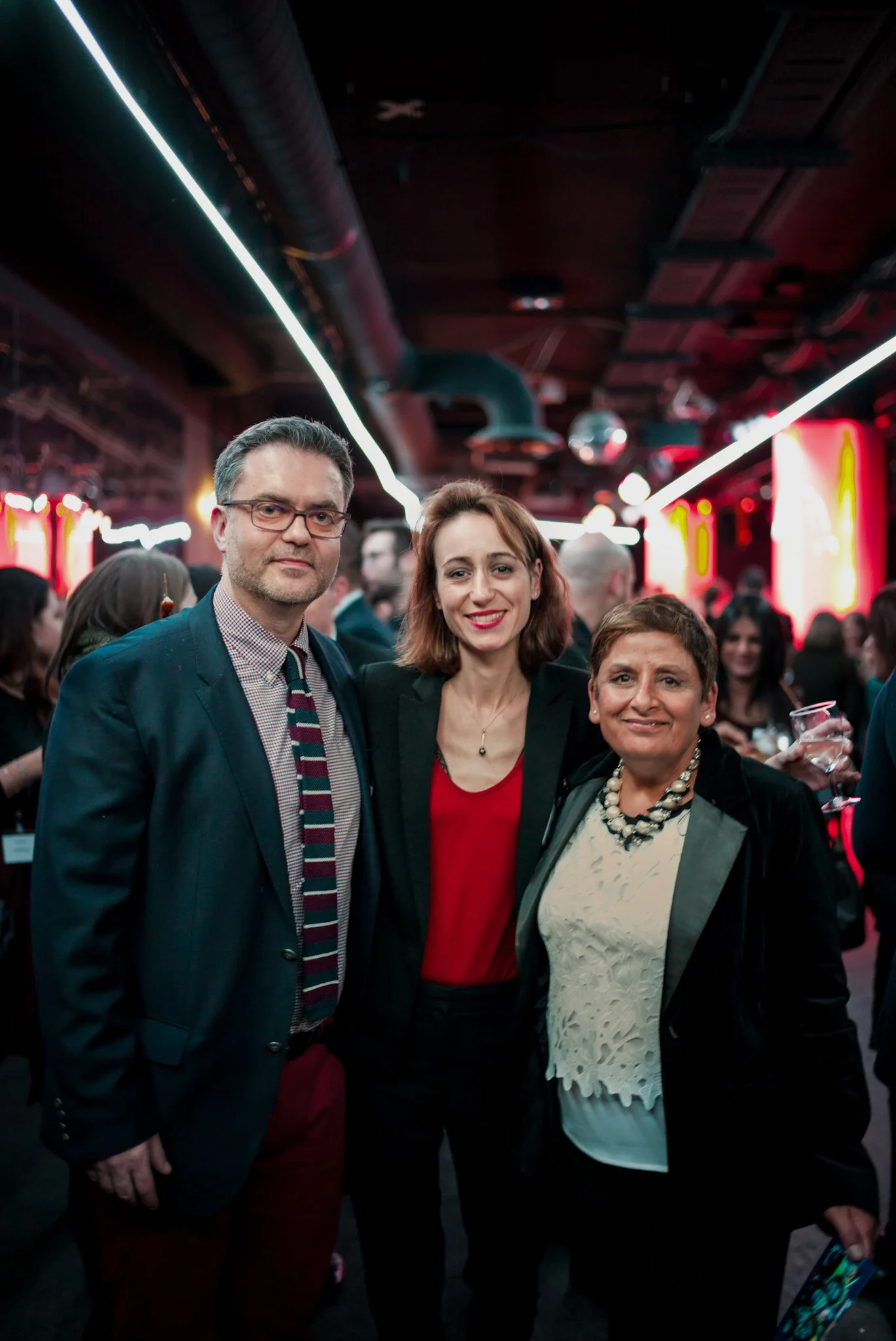 Trois professionnels posent ensemble lors de la soirée annuelle Régus. Tenues élégantes, sourires chaleureux et décor industriel chic, montrant l'esprit d'équipe et de réseautage de l'événement.