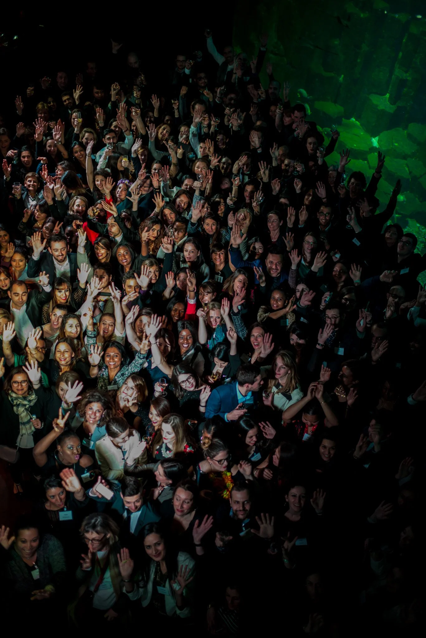 Vue aérienne de la foule lors de la soirée Régus Paris. Invités levant les mains et souriant, ambiance électrique et festive, capturant l'énergie collective et l'enthousiasme de l'événement.