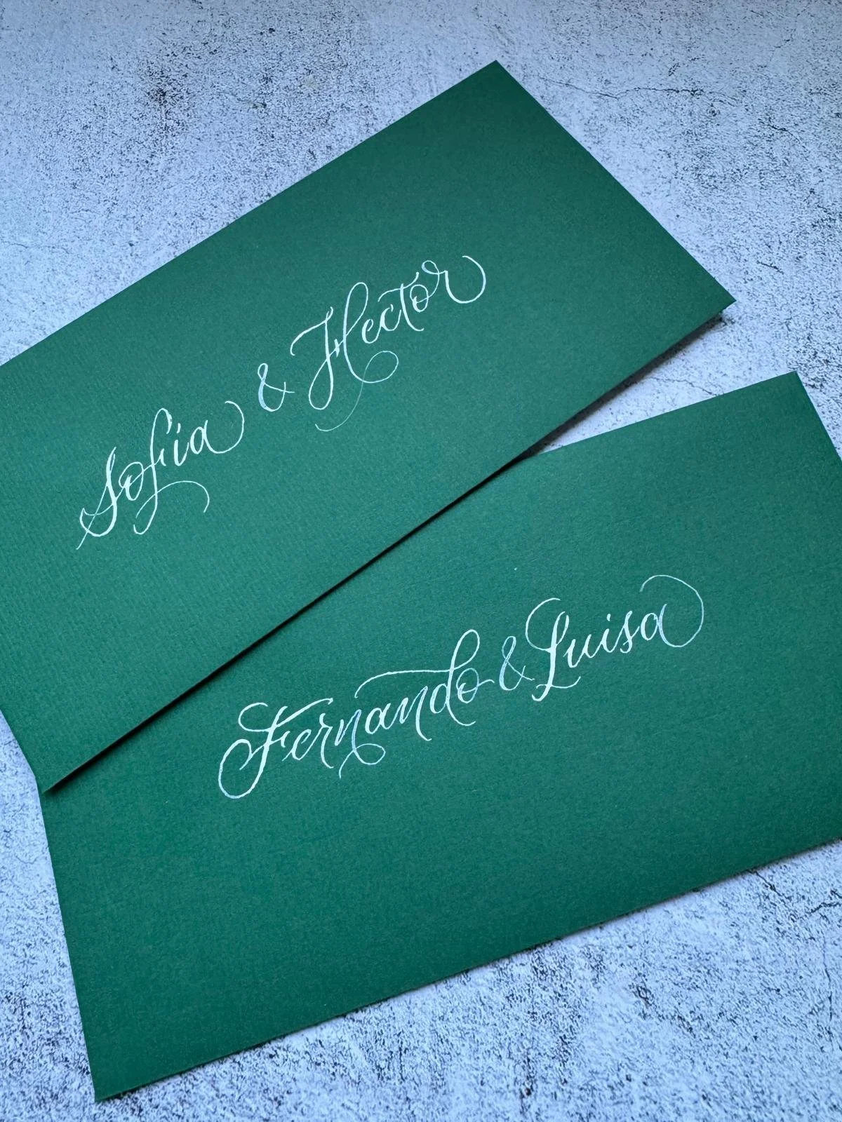 Tarjetas verdes con escritura en letra cursiva blanca para una boda personalizada. Caligrafía personalizada por Bendita Caligrafía.