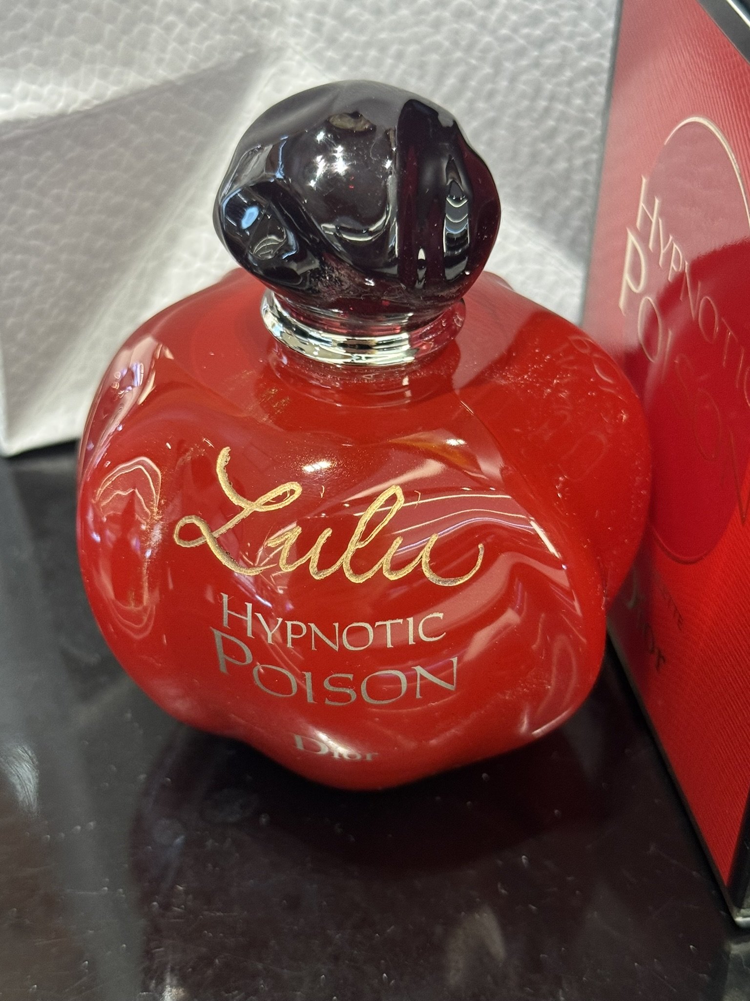 Botella de perfume con tapa de color negro de marca Dior y envase rojo con letras grabadas en caligrafía dorada.